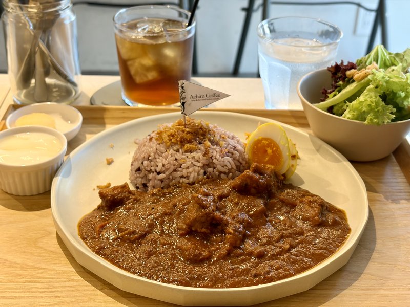 Achim Coffeeのトマトチキンカレー。とろりとしたルーに鶏肉がごろごろ、紫がかった穀物米と半熟のゆで卵が添えられている