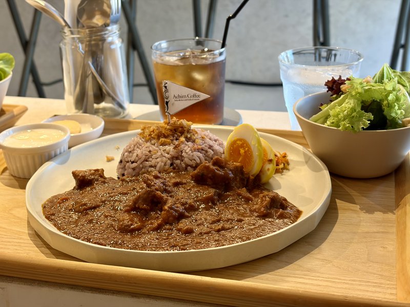 Achim Coffeeのランチプレート。トレーにスパイスカレーと穀物米、半熟のゆで卵、有機野菜サラダ、烏龍茶
