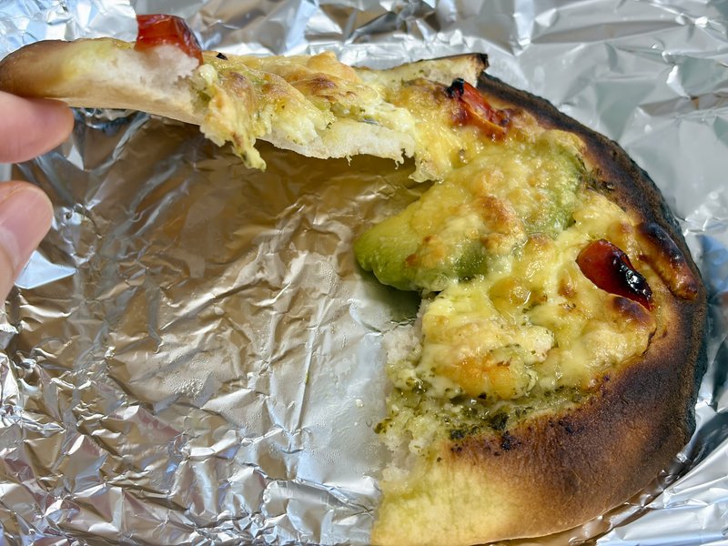 Baker thetaの米粉ピザを一切れ持ち上げたところ。チーズが伸びて、生地の断面が見えている