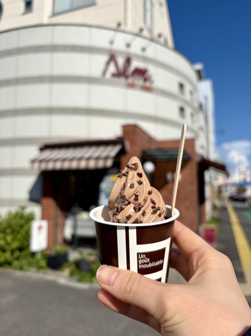 スイス菓子アルムのオリジンカカオソフト。店舗を背景に持ったところ