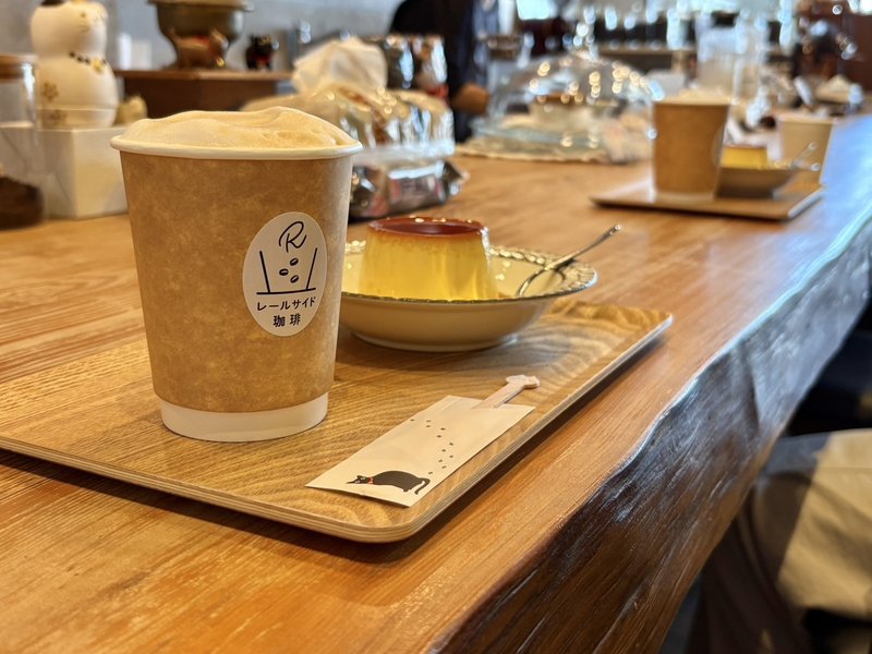 レールサイド珈琲のカウンター席。一枚板のカウンターに、コーヒーとプリンをのせた木のトレーが並ぶ