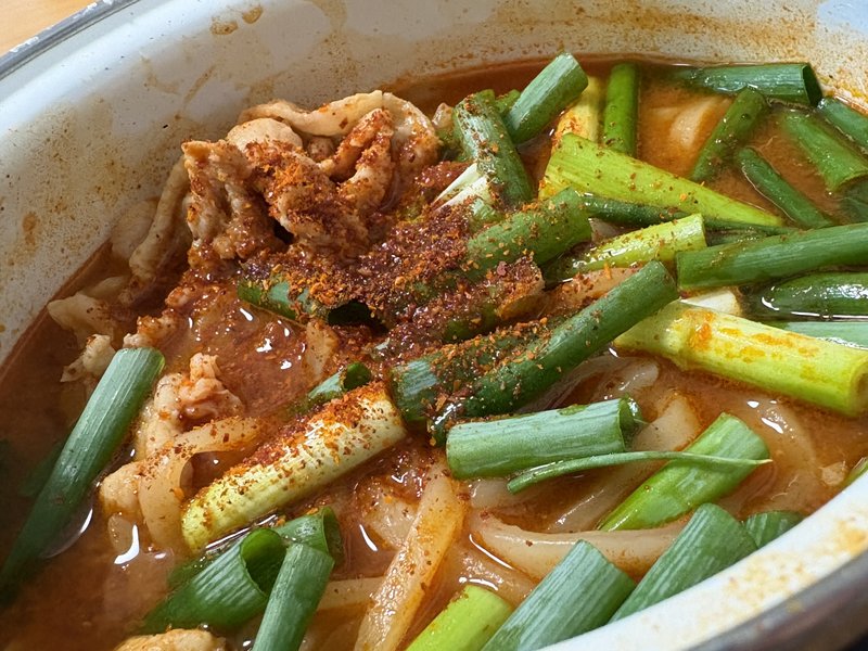 家で作った夜叉うどんのアップ。赤いスープに青ネギと豚肉、唐辛子粉末がかかっている